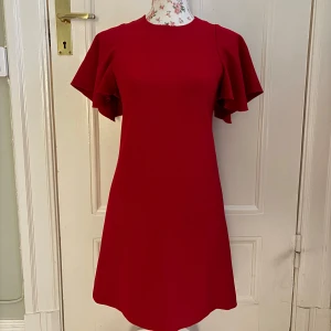 Röd klänning från Maje  - Säljer den här supersnygga röda klänningen från Maje, i storlek S. Klänningen har superfina volangärmar och dragkedja i ryggen. Den har aldrig blivit använd och är i nyskick men utan prislapp. Perfekt klänning nu till jul. Säljer för att den inte kommit till användning. 