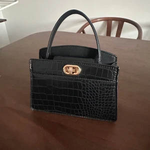 Svart handväska med krokodilmönster - Snygg svart mini handväska med krokodilmönster från H&M har även ett längre band som följer med