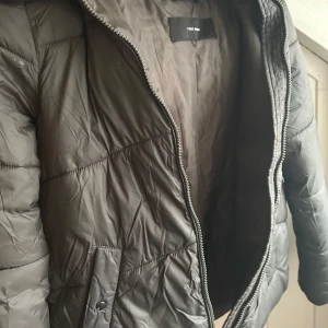  pufferjacka från Vero Moda - Snygg olivgrön pufferjacka från Vero Moda med dragkedja och huva.  Jackan har en stilren look och praktiska fickor framtill. Den sitter jätte fint på!  