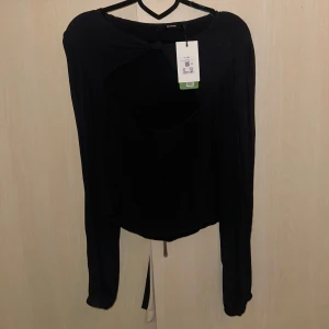 Svart långärmad topp från Bikbok - Snygg svart långärmad topp från Bikbok med en unik cut-out detalj framtill. Perfekt för en stilren look. Toppen är i ett mjukt och bekvämt material.