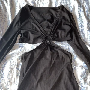 Svart ribbad klänning med knytning - Trendig svart klänning med ribbad textur och unik knytning framtill. Klänningen har långa ärmar.