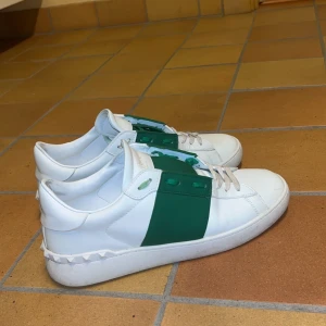Valentino Garavani sneakers i vitt och grönt - Snygga Valentino Garavani sneakers i vitt o grönt. Har haft i en månad och högra skon har en liten defekt på tån men annars är dom fina