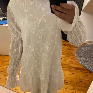 Vit blommig klänning från NA-KD - Säljer en söt och snygg vit klänning från NA-KD med blommigt mönster och volangdetaljer. Klänningen är perfekt inför sommaren alla olika tillfällen! Klänningen har långa ärmar och öppen rygg som man kan knyta. Aldrig använd, med prislapp på. I storlek 34