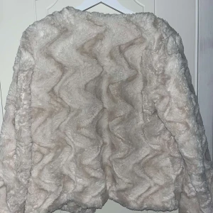 Beige pälsjacka från Vero Moda - Säljer en fluffig och stilren beige pälsjacka från Vero Moda. Jackan har en snygg struktur och stängs med knappar framtill. Perfekt för att hålla sig varm och trendig. Jackan är endast använd 1 gång, det är ljuset som gör så att den ser smutsig ut den är ren i verkligheten