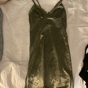 Olivgrön sidenklänning - Elegant olivgrön klänning i siden med smala axelband och knytning framtill. Perfekt för en stilren look. 