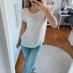 Vit blus med volangdetaljer - Säljer en söt vit blus med volangdetaljer på ärmarna. Blusen är ärmlös och har en luftig passform, perfekt för varma dagar. Den är enkel att matcha med både jeans och kjol.