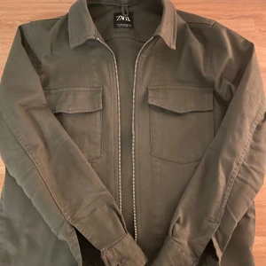 Grön overshirt från Zara - Snygg grön overshirt från Zara med dragkedja och två bröstfickor. Perfekt för lager-på-lager-stil. Passar bra till både jeans och t-shirt.