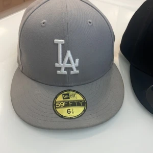 New Era kepsar med broderade logotyper - Säljer flera New Era kepsar med broderade logotyper. Grå keps med vit LA-logga, svart keps med röd NY-logga, svart keps med vit Sox-logga och hjärtdetalj, samt blå keps med vit LA-logga och färgglada broderier på sidan. 