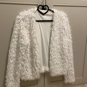 Vit fluffig cardigan  - Säljer en fluffig vit cardigan med långärmad design. Perfekt för att hålla sig varm och snygg över festklänningen eller bara en snygg detalj till outfiten. 60 cm lång från axlarna och ner. 