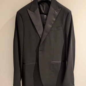 Svart smoking från Mango i stl 50/48 - Elegant svart smoking från Mango. Kavajen har en slim fit passform i stl 50, medan byxorna är stl 48. Finns sömsmån för skräddarändringar. Endast använd en gång. Perfekt för nyårsfirandet!