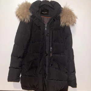 Svart dunjacka från Hollies stl 34 - Säljer en snygg svart dunjacka från Hollies med avtagbar pälskant på huvan. Jackan har dragkedja och knappar framtill samt praktiska fickor. Perfekt för kalla vinterdagar.            Nypris var 4999kr och priset kan diskuteras. Skriv gärna om du behöver måtten eller om du vill ha fler bilder.                                                 Andra bilden tillhör inte mig utan det är en bild jag hittat på nätet för att demonstrera passformen 