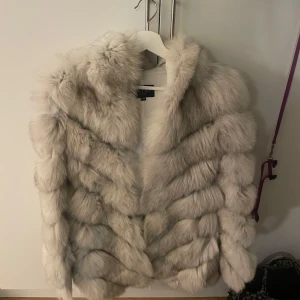 Beige pälsjacka - Säljer en lyxig beige pälsjacka med fluffig textur. Jackan har en elegant design och är perfekt för att hålla dig varm under kyliga dagar. Den är stilren och passar till många olika outfits.