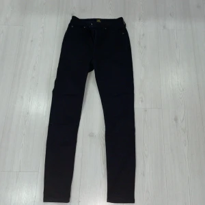 Svarta jeans från Lee - Snygga svarta jeans från Lee med en klassisk design. De har en smal passform och är perfekta för en stilren look. Jeansen har knappar och dragkedja framtill. Storleken är W27 och L31