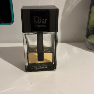 Dior Homme Intense parfym - Säljer en elegant Dior Homme Intense parfym i en stilren glasflaska med svart lock. Doften är intensiv och maskulin, perfekt för den som vill sticka ut. Flaskan har en modern design med en tydlig logotyp på toppen. Inköps pris 1250 45 procent kvar 600kr pris kan diskuteras 
