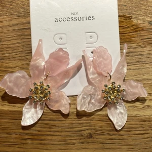 Rosa blommiga örhängen från NLY Accessories - Stora och iögonfallande rosa örhängen i form av blommor från NLY Accessories. De har en glittrig detalj i mitten som ger en extra touch av glamour. Fått väldigt många fina kommentarer när jag haft dom, köpta på Nelly i stockholm