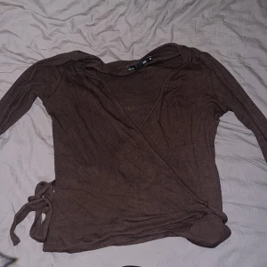 Jätte bra tröja använder it längre köpte den för två dagar sen och jag klippte lite snörarna för dom var för långa men den funkar bra - Säljer en brun omlottopp med långa ärmar och knytband i sidan. Perfekt för lager-på-lager och ger en stilren look. Passar bra till både jeans och kjol.