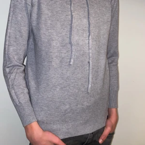 Merinoull Hoodie - Snygg och enkel grå hoodie med dragsko i halsen. Perfekt om man har ”grisch” stilen. Det finns en liten fläck i mitten av hoodien men går förmodligen att tvättas bort