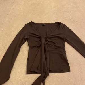 Brun långärmad topp med knyt - Säljer en brun långärmad topp från Gina Tricot med knyt framtill. Toppen har en v-ringad design och är perfekt för höstgarderoben. Den är helt ny, använt den bara 2 gånger. I storlek XS. Helt ny!