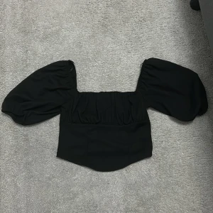 Svart topp från Gina Tricot - Snygg svart topp från Gina Tricot med puffiga ärmar och en fyrkantig urringning. Perfekt för en stilren look.