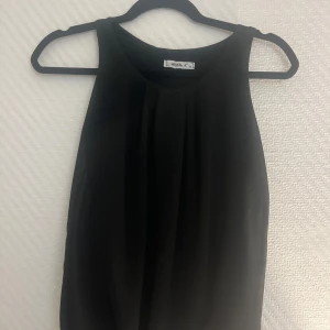 Svart ärmlös topp från MyHollys - Snygg svart ärmlös topp från MyHollys i storlek XS. Perfekt för både vardag och fest med sin stilrena design. Toppen har en elegant öppen ryggdetalj som ger en extra touch. Passar utmärkt till både jeans och kjol!