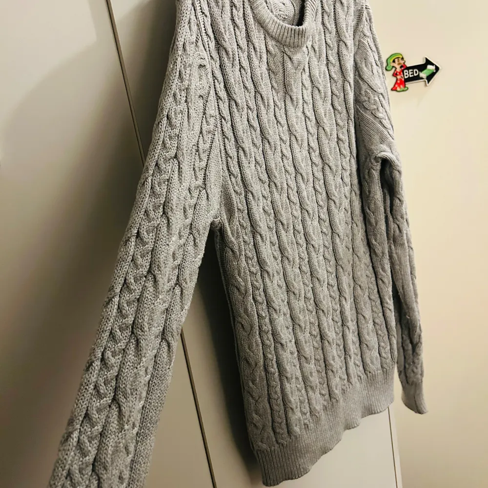Säljer en snygg grå stickad tröja från 157 i storlek S. Den har ett klassiskt flätmönster och är perfekt för kyliga dagar. Tröjan är långärmad och har ribbade muddar vid ärmslut och nederkant. Supermysig och stilren för både höst och vinter!. Neuletakit & Villapaidat.
