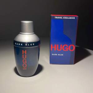 Säljer en flaska Hugo Dark Blue parfym, perfekt för resor. Flaskan är stilren med en mörkblå färg och silverdetaljer. Kommer i en snygg förpackning med samma färgtema. Perfekt för den som vill ha en fräsch och maskulin doft. Passa på att köpa denna exklusiva doft!