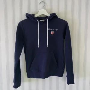 Mörkblå hoodie från GANT - Säljer en snygg mörkblå hoodie från GANT. Perfekt för både vardag och chill. Den är i bra skick och säljer då den blivit för liten! 