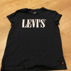 Svart t-shirt från Levi's - Säljer en klassisk svart t-shirt från Levi's i storlek S. Den har en vit logga på bröstet och är gjord i mjukt bomullsmaterial. Perfekt för vardagsbruk och kan enkelt matchas med jeans eller shorts. T-shirten är kortärmad och i nyskick.