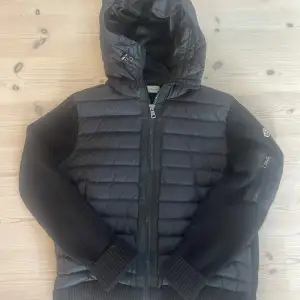 Säljer en snygg svart jacka från Moncler i storlek L. Jackan har en quiltad design med dragkedja och en mysig huva. Ärmarna är stickade och den är varm. Kondition 10/10 inte min stil