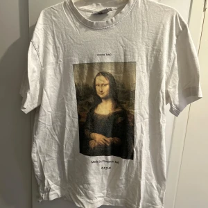 Vit t-shirt med Mona Lisa-tryck från A.P.O.H - Säljer en cool vit t-shirt från A.P.O.H med ett stort tryck av Mona Lisa på framsidan. T-shirten är i bomull och har en normal passform. Perfekt för dig som vill ha en konstnärlig touch i garderoben! 🖼️