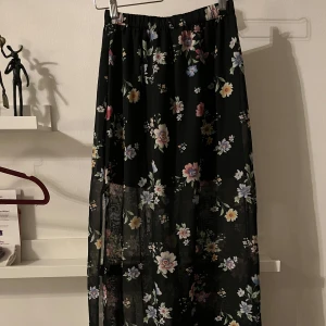 Blommig långkjol från H&M - Säljer en superfin blommig långkjol från H&M i storlek XS. Kjolen är svart med ett färgglatt blommönster och har en elastisk midja för extra komfort. Perfekt för både vår och sommar! 🌸Kort svart underkjol med skir långkjol 