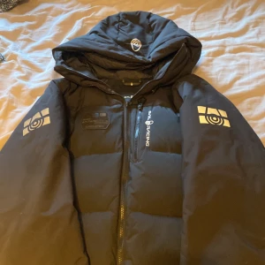 Svart dunjacka från Sail Racing storlek M - Säljer en svart dunjacka från Sail Racing i mycket bra skick. Jackan har en fyllning av ansvarsfullt källad dun med 500 fill power. Den har en dragkedja framtill och en justerbar huva. Perfekt för kalla vinterdagar! ❄️ den har inga hål och 10/10 skick Ny 4200kr Pris kan förhandlas storlek Medium