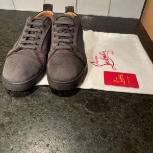Grå sneakers från Christian Louboutin - Säljer ett par grå sneakers från Christian Louboutin med den ikoniska röda sulan. De är i skinn inuti skon med en stilren design. Perfekta för både vardag och fest! Skorna är pyttelite sönder i hälen på båda skor och på den ena skon är skosnöret lite sönder i slutet men detta räknas då med i priset. Jag säljer dessa pågrund av att de är för små och kommer aldrig till användning. De kommer med dustbag och en Christian Louboutin kort. Messa gärna om det finns frågor om skorna. 