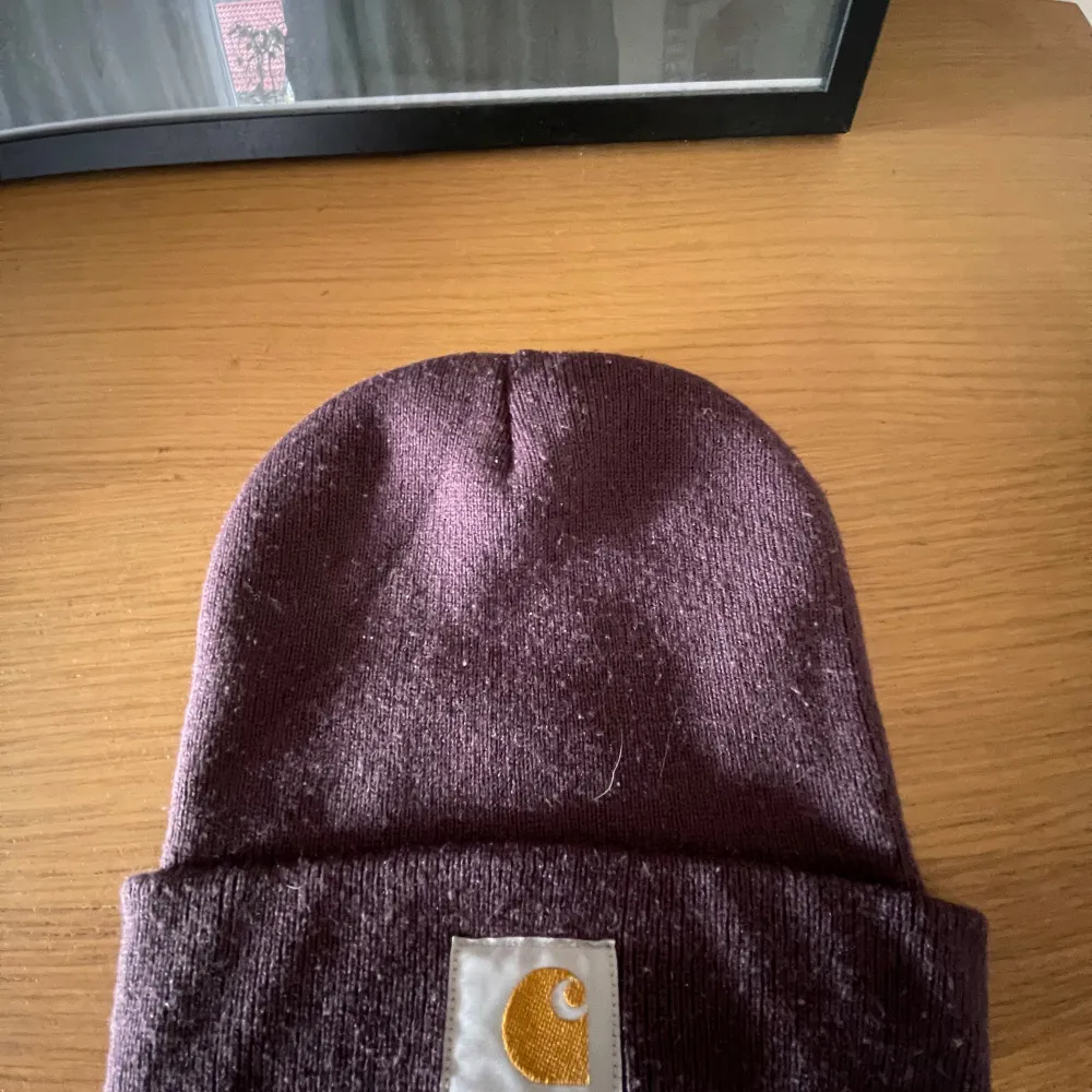 Säljer en snygg lila mössa från Carhartt i nytt skick. Den är stickad och har en broderad logga framtill. Perfekt för att hålla sig varm under höst och vinter. One size fits all, så den passar de flesta. Grym accessoar för både vardag och fest!. Asusteet.