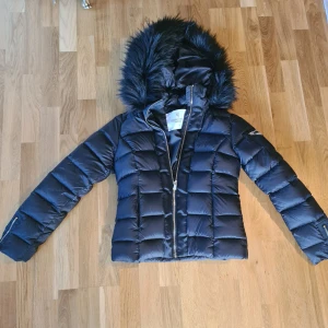 Svart dunjacka med päls Chiara Forti - Säljer en riktigt snygg svart dunjacka från Chiara Forthi med pälsdetaljer på huvan. Perfekt för kalla vinterdagar och håller dig varm och stilren. Passar både till vardags och festliga tillfällen. Som ny då den endast är använd fåtal ggr. 