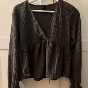 -brun  ribbad blus -  brun blus med ribbad textur och v-ringning. Den har långa ärmar och en lätt volangdetalj vid midjan. 