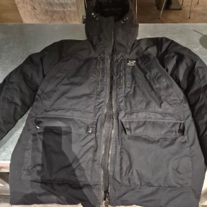 Svart jacka från RevolutionRace - Säljer en svart jacka från RevolutionRace med dragkedja och flera praktiska fickor. Jackan har en hög krage och är perfekt för kyligare väder.