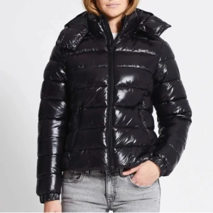 Svart moncler liknanade pufferjacka - Snygg svart pufferjacka med dragkedja och huva. Perfekt för kyliga dagar med sin glansiga yta och vadderade design. Jackan har långa ärmar och en modern look. Väldigt lik moncler maya modellen. Jackan är helt oanvänd och är i nyskick. Strl S.🥰❤️
