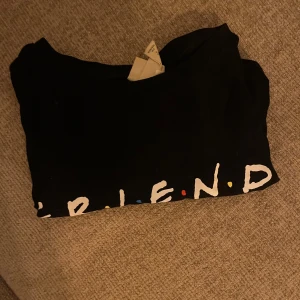 Svart t-shirt med Friends-tryck från H&M - Snygg svart t-shirt från H&M med det ikoniska Friends-trycket på framsidan. Baksidan har roliga citat från karaktärerna i serien. Perfekt för alla Friends-fans!