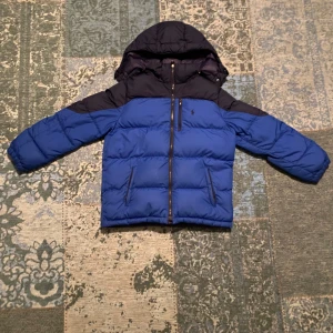 Blå och marinblå dunjacka med huva - Snygg blå och marinblå dunjacka från Polo Ralph Lauren med huva och dragkedja. Perfekt för kyliga dagar med sin quiltade design och långa ärmar.  Priset kan diskuteras 