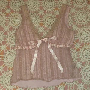 Rosa spetslinne från Venus London - Säljer ett romantiskt rosa spetslinne från Venus London. Linnet har en vacker rosett framtill och volangdetaljer vid bysten. Perfekt för en söt och feminin look. Har ett hål från en säkerhets nål på baksidan men väldigt litet och syns knappt 