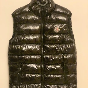 Svart dunväst från Moncler - Snygg svart dunväst från Moncler med glansig yta och dragkedja framtill. Västen har en hög krage och Moncler-logga på bröstet. Perfekt för kyliga dagar.