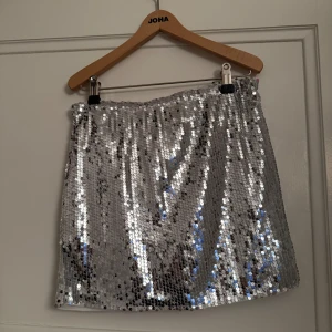 Glittrig silverkjol - Snygg och glittrig silverkjol täckt med paljetter. Perfekt för att sticka ut på festen. Kort modell som ger en trendig look. Perfekt till nyår