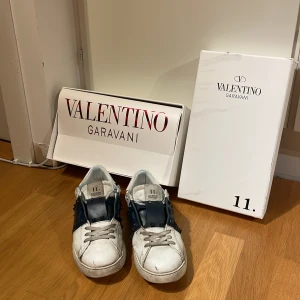 Valentino Garavani sneakers - Snygga Valentino Garavani sneakers i vitt med mörkblå detaljer. Några av spikarna saknas då dom har sparkats av. Skorna har inga defekter och inte haft de så länge. Box o allt ingår  