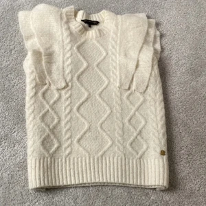 Vit stickad tröja från Pernilla Wahlgren - Säljer en stilren vit stickad tröja från Pernilla Wahlgren. Tröjan har ett vackert flätmönster och volangdetaljer på axlarna. Perfekt för kyliga dagar.