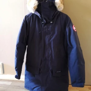 Canada Goose Langford Parkas Navy Blue storlek Small.  - En Canada Goose jacka i marinblå färg. Jackan har en avtagbar huva med pälskant. Jackan har två fickor framtill och två fickor längs sidan av ”bröstkorgen” och 2 innerfickor. Jackan är i väldigt gott skick, använd med omsorg.  Köpt Januari 2021, digitalt kvitto finns.