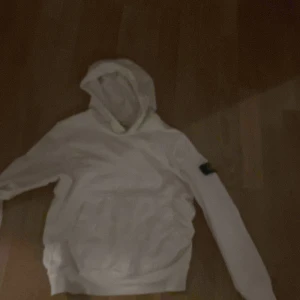 Vit hoodie från Stone Island - Säljer en stilren vit hoodie från Stone Island med deras ikoniska märke på ärmen. Perfekt för en avslappnad look. Hoodien har en klassisk design med huva och långa ärmar.