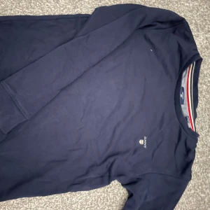 Mörkblå långärmad tröja från Gant - Säljer en stilren mörkblå långärmad tröja från Gant med broderad logga på bröstet. Perfekt för en avslappnad och snygg look. Tröjan har en klassisk rund halsringning och är tillverkad i mjukt material.