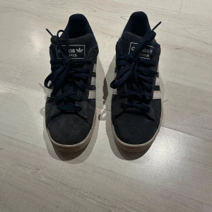 Mörkblåa Adidas Campus sneakers - Säljer ett par svarta Adidas Campus sneakers med vita detaljer och klassiska tre ränder på sidan. Skorna har snörning och en vit sula. Perfekta för en avslappnad stil. Köpta från Zalando. Nypris 1280 kr. Priset kan diskuteras☺️
