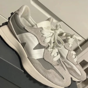 Grå och vita new balance sneakers - Snygga grå och vita sneakers med snörning och en unik sula med mönstrade knoppar. Perfekta för en avslappnad stil.